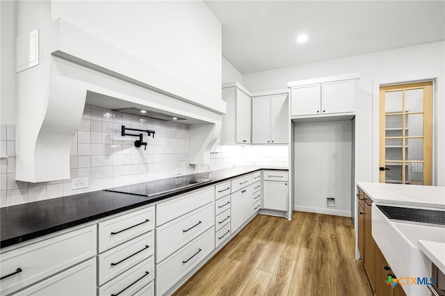 kitchen featuring light hardwood / wood-style flooring, backsplash, black electric cooktop, and white cabinets