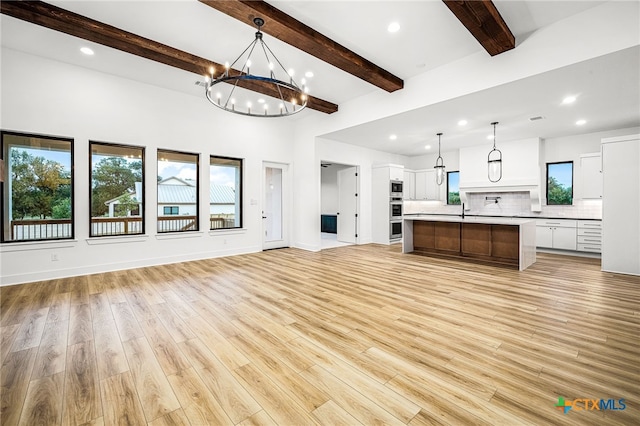 kitchen featuring a kitchen island with sink, light wood-type flooring, hanging light fixtures, and a notable chandelier