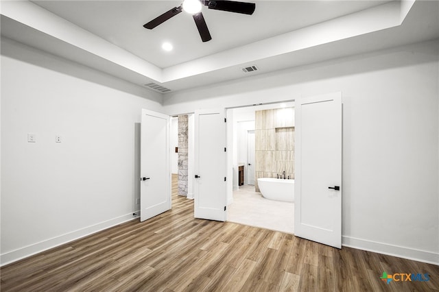 unfurnished bedroom with wood-type flooring, a raised ceiling, ceiling fan, and ensuite bathroom