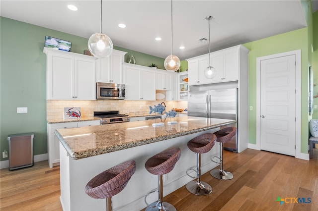 kitchen featuring white cabinetry, appliances with stainless steel finishes, hanging light fixtures, and light hardwood / wood-style floors