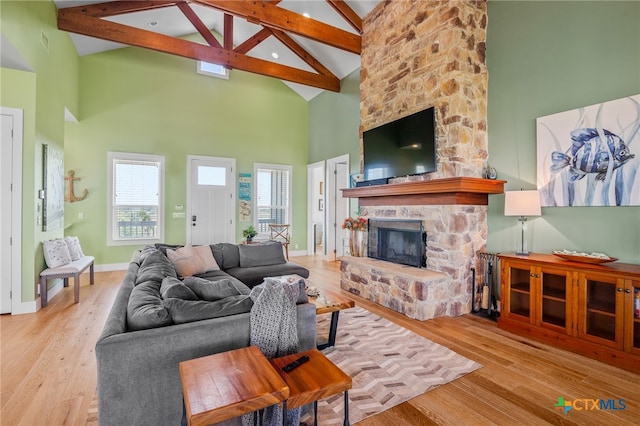 living room with beamed ceiling, a stone fireplace, light wood-type flooring, and high vaulted ceiling