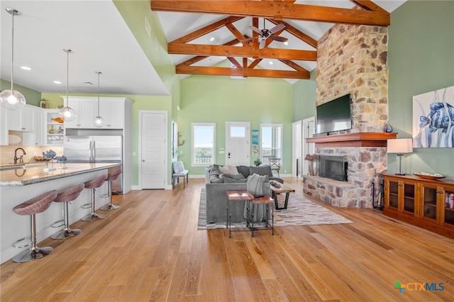 living room featuring ceiling fan, beam ceiling, high vaulted ceiling, a fireplace, and light wood-type flooring