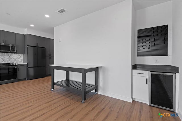 kitchen featuring tasteful backsplash, wine cooler, stainless steel appliances, and light wood-type flooring