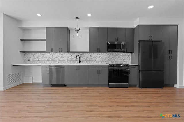 kitchen featuring appliances with stainless steel finishes, backsplash, light hardwood / wood-style floors, and pendant lighting