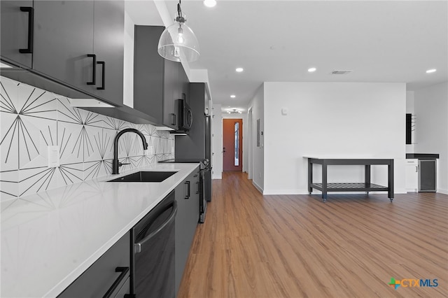 kitchen featuring sink, backsplash, light hardwood / wood-style floors, pendant lighting, and appliances with stainless steel finishes