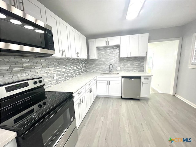 kitchen with a sink, stainless steel appliances, tasteful backsplash, light wood-style flooring, and white cabinetry