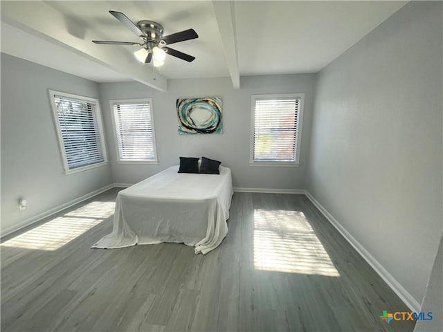 bedroom with baseboards, multiple windows, beamed ceiling, wood finished floors, and ceiling fan