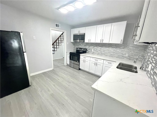 kitchen with decorative backsplash, appliances with stainless steel finishes, light wood-style floors, white cabinetry, and a sink