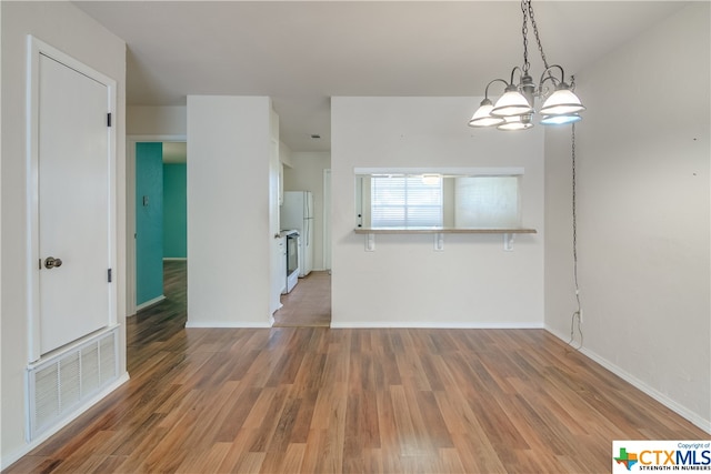 unfurnished dining area featuring wood-type flooring and an inviting chandelier