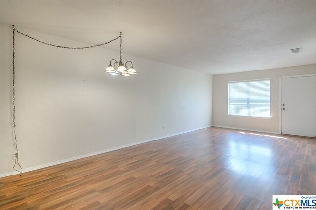 unfurnished room with wood-type flooring and an inviting chandelier