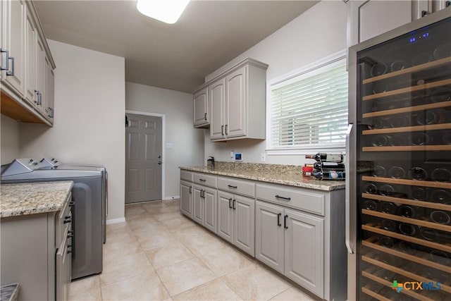 kitchen with gray cabinetry, wine cooler, washer and dryer, light stone countertops, and light tile patterned flooring