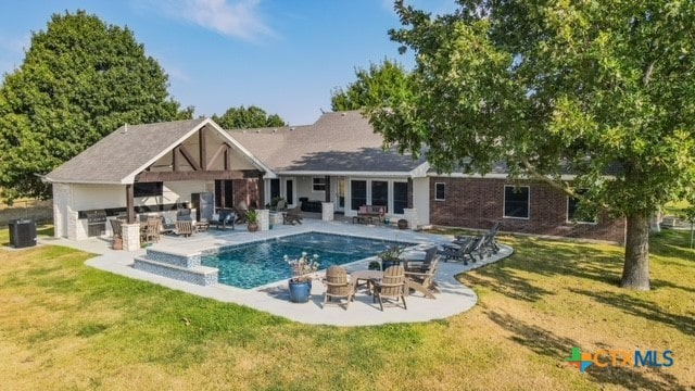 view of pool with a yard, an outdoor kitchen, an outdoor living space, central AC unit, and a patio area