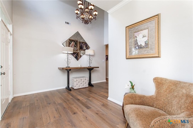 living area with wood-type flooring, ornamental molding, and a chandelier