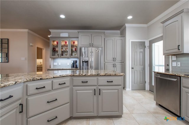 kitchen with stainless steel appliances, tasteful backsplash, light stone counters, light tile patterned floors, and ornamental molding