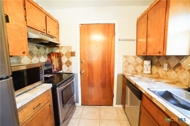 kitchen featuring tile countertops, tasteful backsplash, light tile patterned floors, and stainless steel appliances