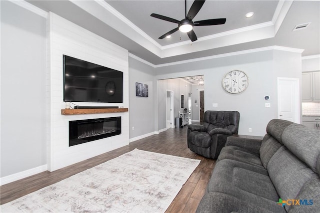 living room with crown molding, a tray ceiling, a fireplace, and dark hardwood / wood-style flooring