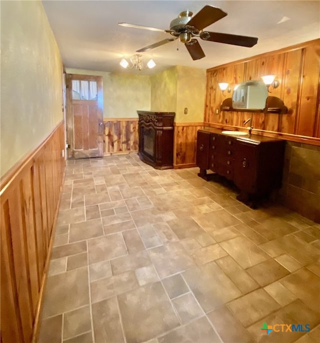 kitchen with a wainscoted wall, wood walls, a fireplace, and a ceiling fan