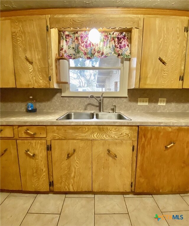 kitchen with tasteful backsplash, light countertops, a sink, and light tile patterned flooring