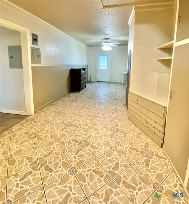 interior space featuring a textured ceiling, ceiling fan, electric panel, stone finish flooring, and attic access