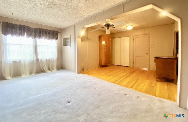 carpeted empty room featuring a ceiling fan, a textured ceiling, and wood finished floors