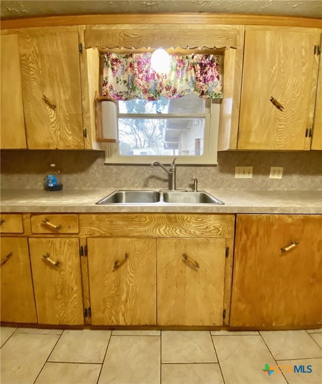 kitchen featuring light countertops, light tile patterned flooring, a sink, and decorative backsplash