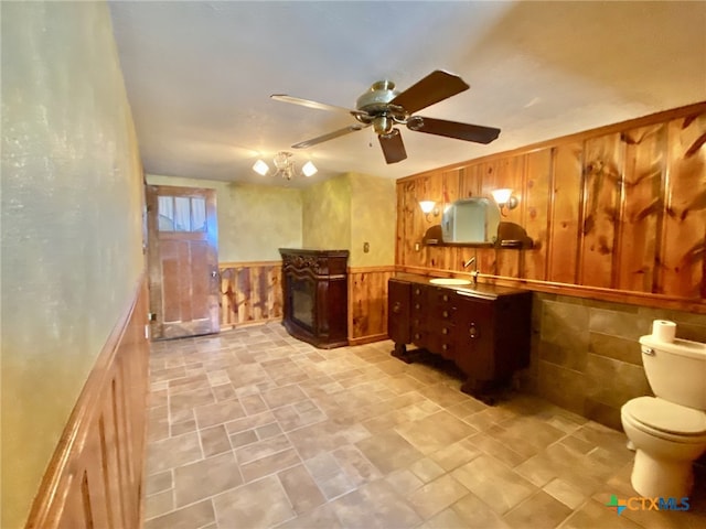 bathroom featuring toilet, wainscoting, wood walls, vanity, and ceiling fan