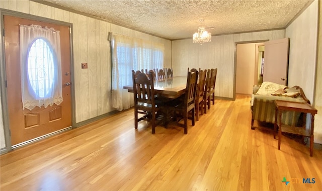 dining space featuring a textured ceiling, light wood-style floors, an inviting chandelier, and crown molding