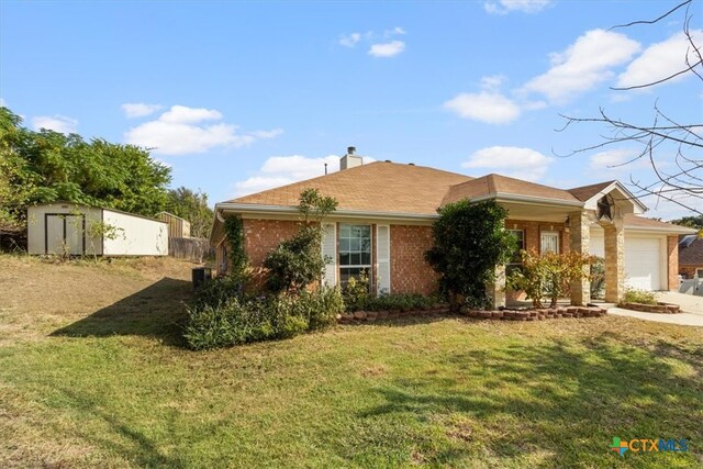 single story home featuring a front yard, a garage, and a storage shed