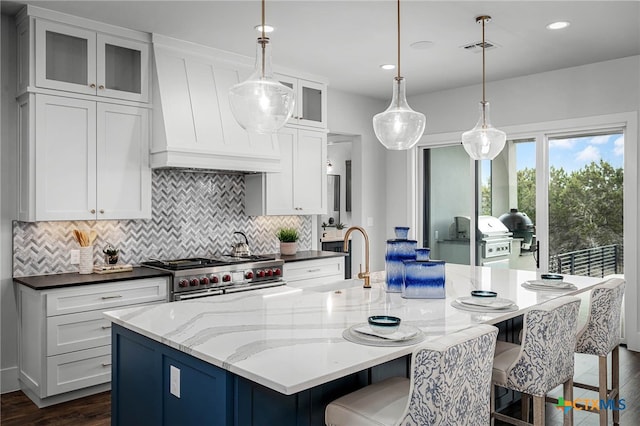 kitchen featuring hanging light fixtures, double oven range, a large island with sink, and white cabinetry