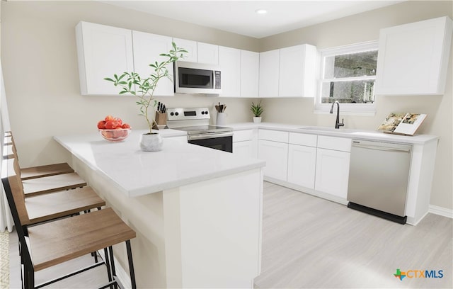 kitchen with a kitchen bar, appliances with stainless steel finishes, kitchen peninsula, sink, and white cabinets