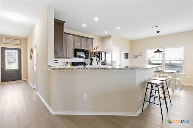 kitchen with light stone counters, dark brown cabinets, black appliances, and light hardwood / wood-style flooring