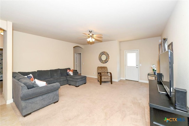 living area with arched walkways, a ceiling fan, baseboards, and light colored carpet