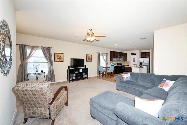 living room featuring healthy amount of natural light, light carpet, baseboards, and ceiling fan