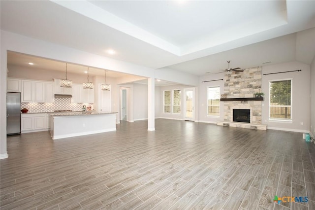 unfurnished living room featuring a ceiling fan, wood finished floors, recessed lighting, a stone fireplace, and baseboards