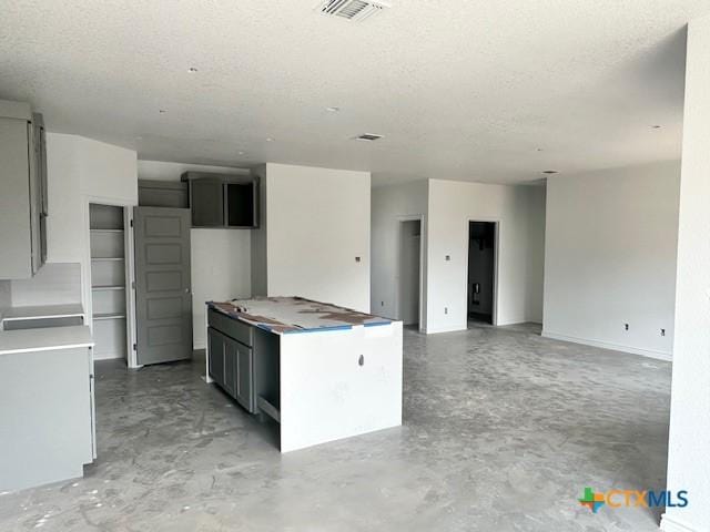 kitchen featuring concrete flooring, a textured ceiling, a kitchen island, and visible vents