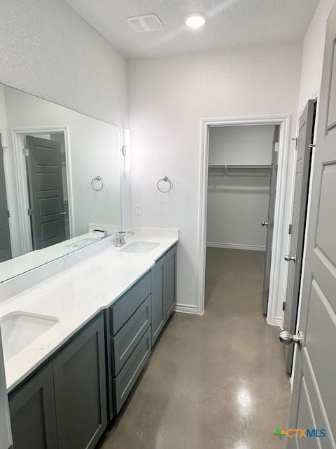 bathroom featuring double vanity, a sink, a walk in closet, and finished concrete floors