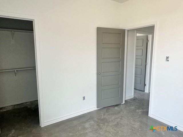 unfurnished bedroom featuring concrete floors, a closet, a walk in closet, and baseboards