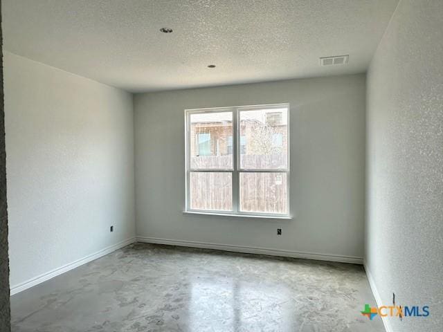 empty room featuring concrete floors, visible vents, a textured ceiling, and a textured wall