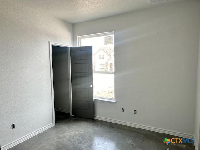 unfurnished bedroom featuring unfinished concrete floors, baseboards, a textured ceiling, and a textured wall