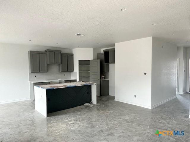 kitchen featuring concrete flooring, backsplash, a kitchen island, and a textured ceiling