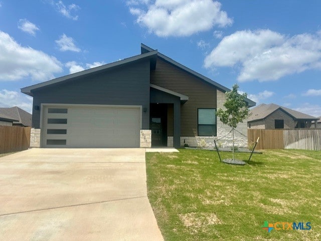 view of front of home with concrete driveway, stone siding, an attached garage, fence, and a front yard