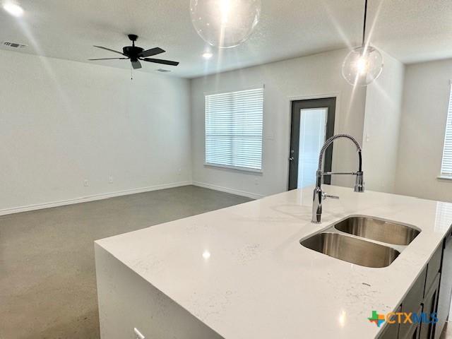 kitchen featuring decorative light fixtures, light stone countertops, open floor plan, and a sink