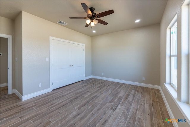 unfurnished bedroom featuring visible vents, baseboards, multiple windows, and wood finished floors