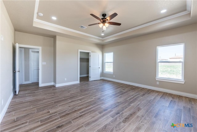 unfurnished bedroom with ornamental molding, a raised ceiling, baseboards, and wood finished floors