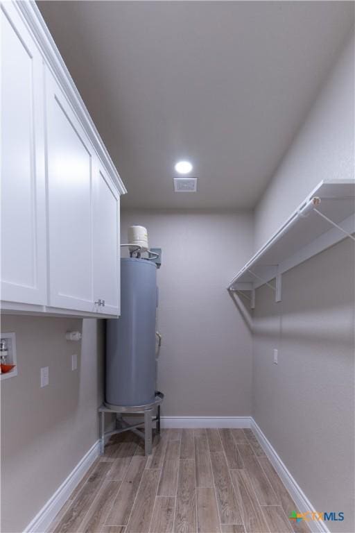 laundry area featuring baseboards, cabinet space, light wood-style floors, and water heater