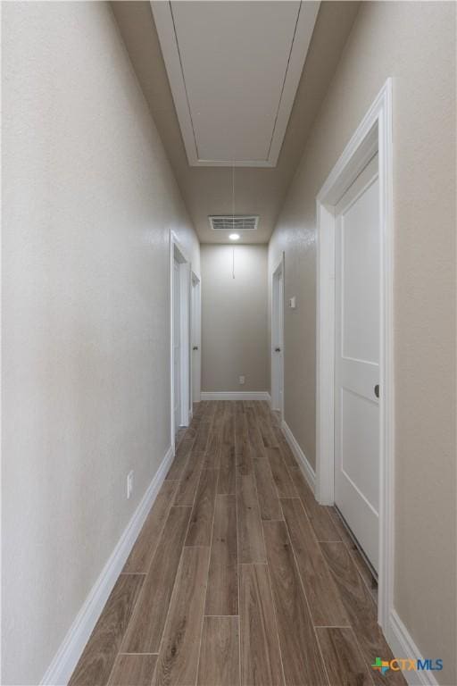 hallway with attic access, wood finished floors, visible vents, and baseboards