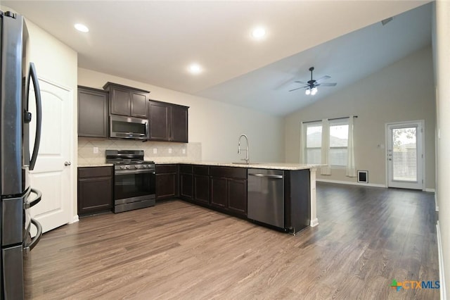 kitchen with appliances with stainless steel finishes, lofted ceiling, wood-type flooring, tasteful backsplash, and dark brown cabinets