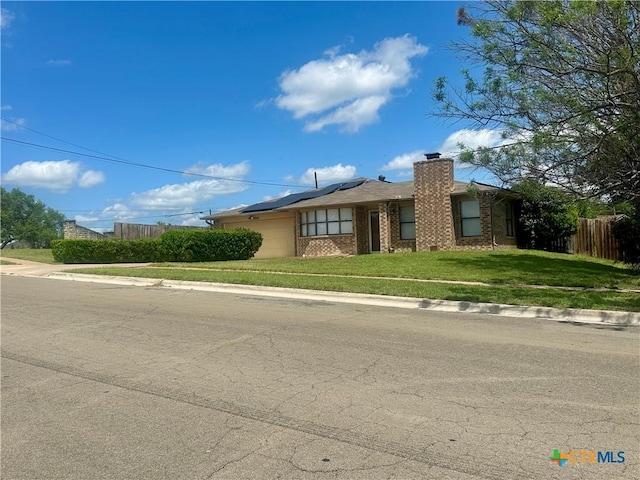 ranch-style house featuring a chimney, fence, solar panels, an attached garage, and a front yard