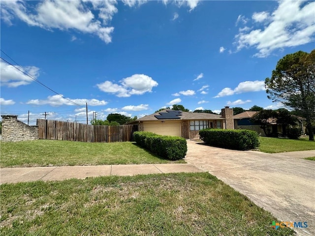 view of home's exterior with fence, brick siding, a garage, a yard, and roof mounted solar panels