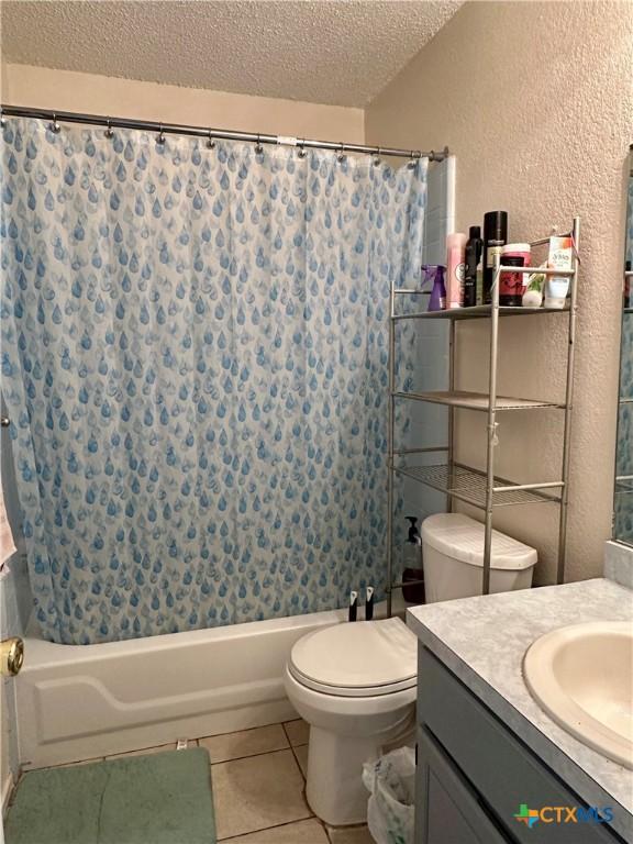 full bath featuring tile patterned floors, shower / bath combo, a textured ceiling, toilet, and a textured wall